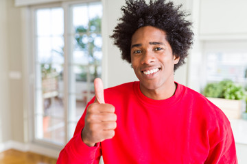 African American man wearing casual red sweatshirt doing happy thumbs up gesture with hand. Approving expression looking at the camera showing success.