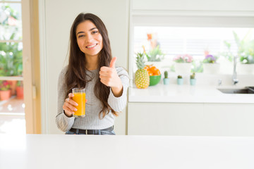 Canvas Print - Young woman drinking a glass of fresh orange juice happy with big smile doing ok sign, thumb up with fingers, excellent sign