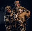 © Fxquadro - Combat conflict, special mission, retreat. Military medic rescues his wounded teammate carrying him off the battlefield. Studio photo against a dark wall