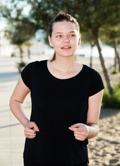 Wall Mural - Smiling adult female in black T-shirt is jogging