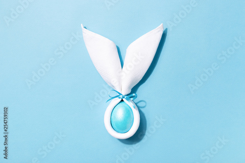 Easter bunny ears made of white napkin with egg on blue background. Minimal s...