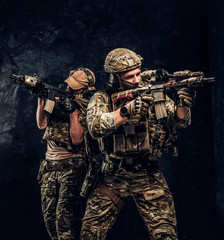 Wall Mural - Two special forces soldiers in full protective equipment holding assault rifles and aiming at the targets. Studio photo against a dark wall.