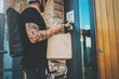 © SFIO CRACHO - Courier city delivery food service at home. Tattooed Man courier delivered the order no name bag with food.