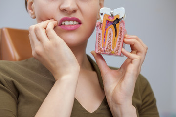 Cropped close up of a woman having toothache holding tooth mold with caries, copy space. Female patient waiting for dental treatment at the clinic. Dentist, health concept