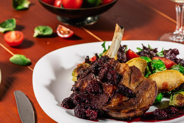 Roasted meat with roast apple, brussel sprouts, cherry tomatoes and salad leaves on a white plate and a glass of white wine, on wooden background