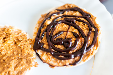 Flat top closeup of rice cake with chocolate drizzle sauce or syrup vegan vegetarian snack dessert one single piece on white plate and peanut butter