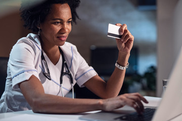 Wall Mural - Smiling black healthcare worker with credit card shopping online.