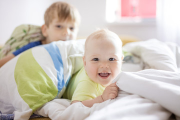 Wall Mural - Baby girl and older brother playing on bed at home. Siblings having fun together.