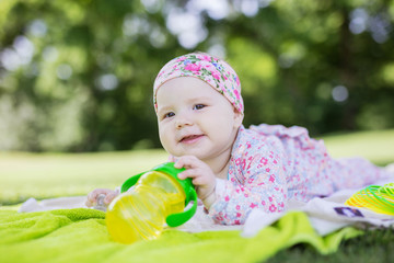 Wall Mural - Cheerful baby girl with bottle of water in summer park