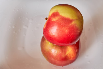 two red ripe apples are lying one on the other on a white plate. fruits and vegetables. vitamin c. energy of nature