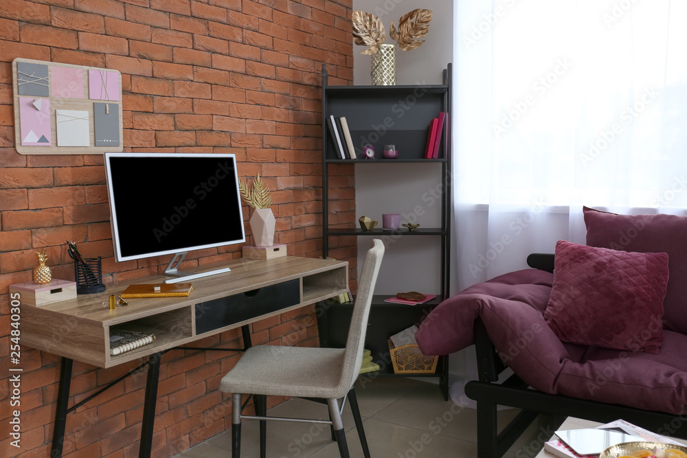 Workplace with modern computer and golden decor near brick wall in room