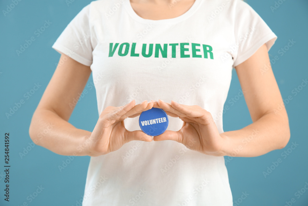 Young female volunteer with badge on color background