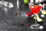 Fototapeta  - Classic alcoholic cocktail cosmopolitan with vodka, liqueur, cranberry juice, lime, ice and orange zest, gray bar counter background, bartender tols, space for text