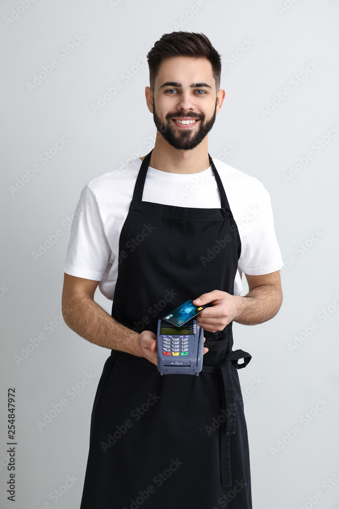 Handsome waiter with payment terminal on light background