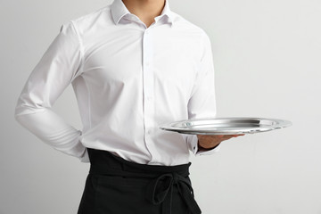 Wall Mural - Handsome waiter with empty tray on light background