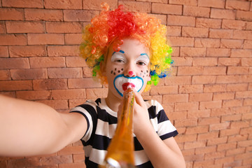 Sticker - Cute little boy with clown makeup taking selfie against brick wall. April fools' day celebration