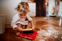 A Small Toddler Girl With Brush And Dustpan Sweeping Floor In The Kitchen At Home.