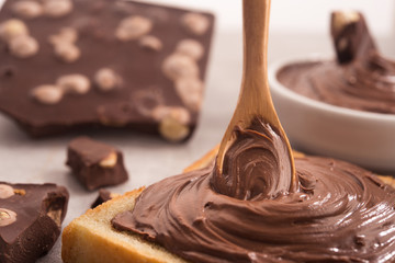 Chocolate spread on slice of bread with spoon, melted cream white bowl