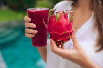 Wall Mural - Close up glass of dragon fruit smoothie and fruit in woman hands