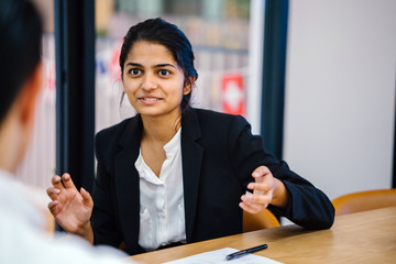 Wall Mural - A beautiful Indian woman is chatting with a colleague inside a conference room. She is talking very beautifully in her black corporate attire. 