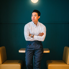 Portrait of a  young, gorgeous hunk Chinese Asian business man in a white long sleeves and black pants. He looks deliberate as he leans against a table in the office pantry during the day. 