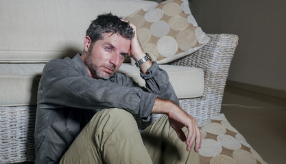 lifestyle portrait young attractive sad and depressed man sitting on living room floor feeling despe