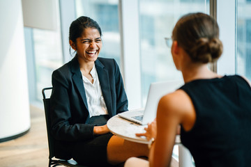 Wall Mural - An exquisite Indian woman sitting by an accomplice inside a cafeteria. She is telling a joke with a teammate.