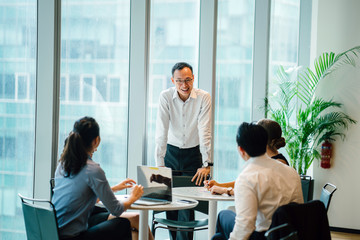 Wall Mural - A young Asian Chinese master is giving a presentation before his partners in the work environment. He is wearing a white polo shirt and dull pants.