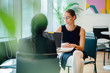 © Danon - A Caucasian white woman has a business meeting (interview) with an Asian woman while checking her email in an office during the day. Image taken with a blurred plant as foreground.