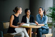 © Danon - Portrait of a diverse group of three professionally dressed young woman (Chinese, Indian and Caucasian) having a casual discussion around a table in a meeting room during the day.