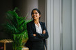 © Danon - Image of a modern Asian Indian businesswoman standing in the office and leaning on a glass window ledge. She laughs and strikes a glamorous pose in front of the camera.
