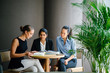 © Danon - A young Indian Asian woman is having a casual business meeting with her team in a conference room. They are sitting and using a notebook as their reference for their new project.