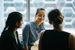 © Danon - Image of a young Chinese Asian woman manager chatting with her team in their office. She smiles back as she listens to her colleague talking about their new project.
