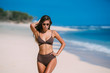 © romannoru - Beautiful tanned girl posing on beach with white sand and blue ocean.