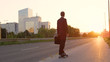 SUN FLARE: Young man in a black suit riding his skateboard into the sunset.