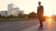 LENS FLARE: Smiling businessman skateboarding down the empty sidewalk at sunset