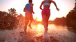 CLOSE UP Unrecognizable woman and man running towards sunset and splashing water