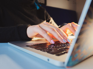 Young business woman working on laptop. Focus on hands typing on keyboard. Sunrise or sunset light leaks