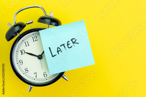 Fotografía Sticky post with handwriting the word Later stick on alarm clock on solid yellow