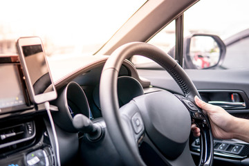 Wall Mural - Male driver hand holding on steering wheel using smartphone for GPS navigation. Mobile phone mounting with magnet on the car console in modern car. Urban driving lifestyle with mobile app technology