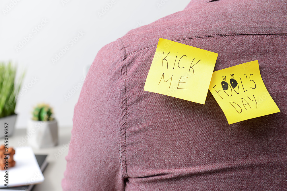 Sticky notes on back of young man, closeup. April Fool's Day prank