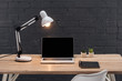 modern workplace with laptop with blank screen, plants, bright lamp and notebook on wooden table near black brick wall