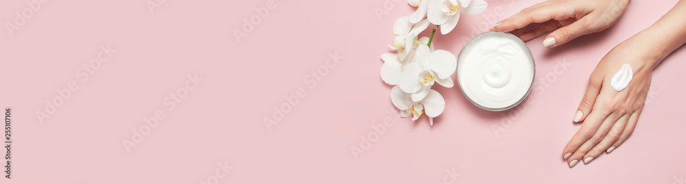 Young woman moisturizes her hand with cosmetic cream lotion opened container with cream body milk White Phalaenopsis orchid flowers on pink background Flat lay top view minimalism style Beauty concept - obrazy, fototapety, plakaty 