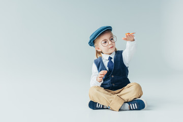 Wall Mural - adorable kid sitting on floor with crossed legs and holding butterfly on grey background