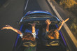 © Fabio Principe - Top view a pair of euphoric women in a convertible car twisting and waving. Two curly girls on vacation having fun driving the auto, laughing happily singing, enjoying freedom in a beautiful sunlight