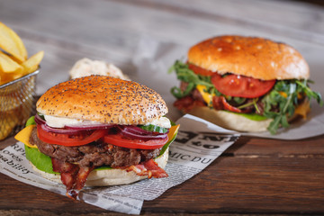 Two fresh classic burgers with beef, cheese, bacon, onion and lettuce in bun with poppy seeds on wooden table.