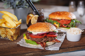 Two fresh classic burgers with beef, cheese, bacon, onion and lettuce in bun with poppy seeds on wooden table.