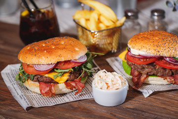 Two fresh classic burgers with beef, cheese, bacon, onion and lettuce in bun with poppy seeds on wooden table.