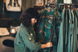 © LUMINA IMAGES - Pretty Asian woman standing by the clothes rack at vintage military shop and folding shirts.