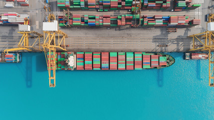 Aerial top view container ship at sea port and working crane bridge loading container to warehouse for logistics, import export, shipping or transportation.